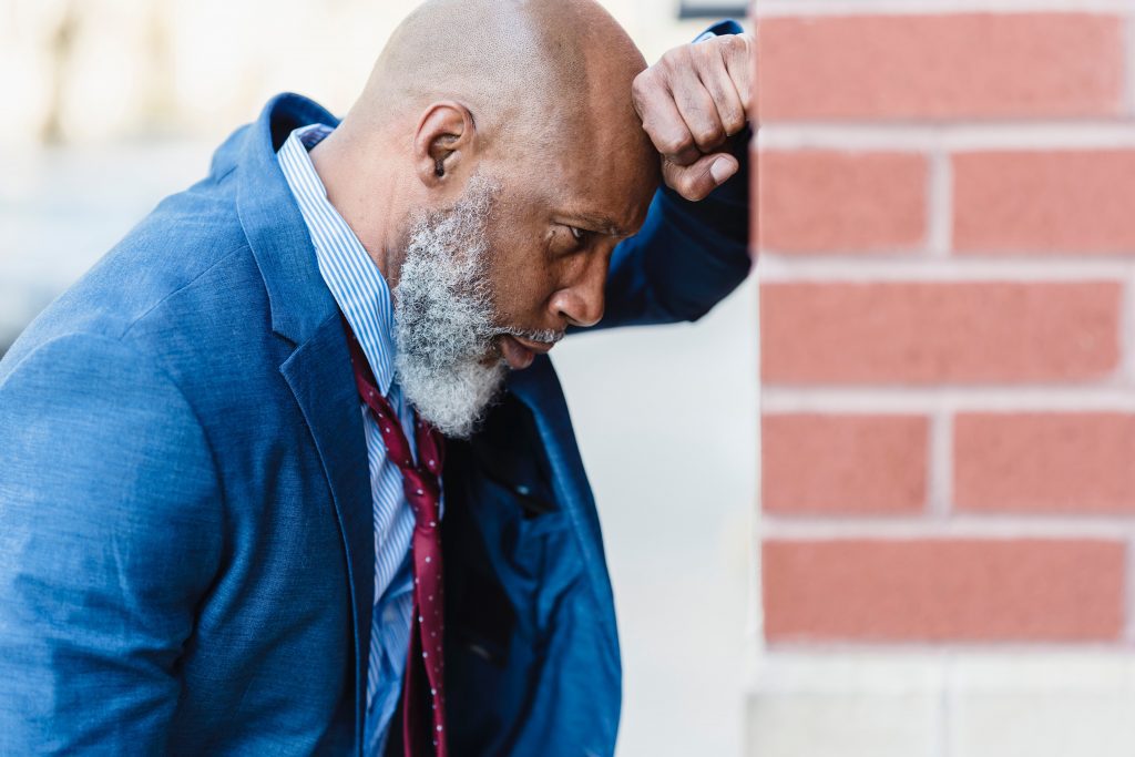 Retarded or Delayed Ejaculation: Older man leans against wall head on hand looking depressed